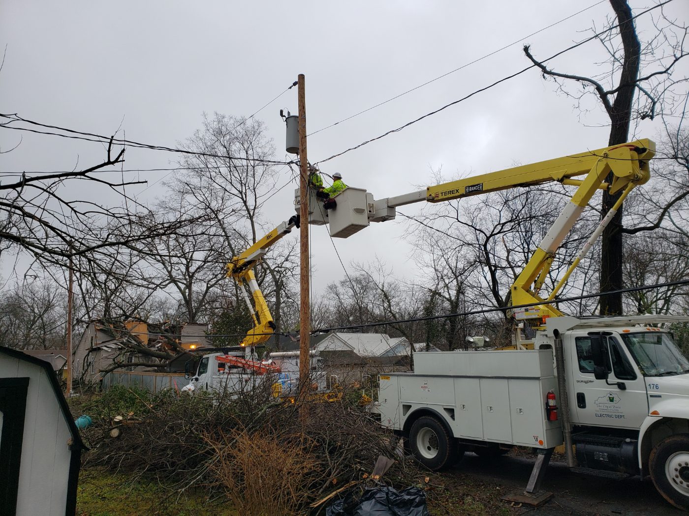 Paris Electric bucket trucks with a line worker raised to a utility pole in a residential area.